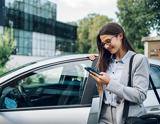 Mujer fuera de un coche, escribiendo en el móvil mientras abre la puerta del vehículo