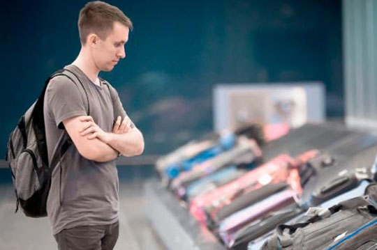 Chico joven con una mochila esperando que su maleta pase por la cinta